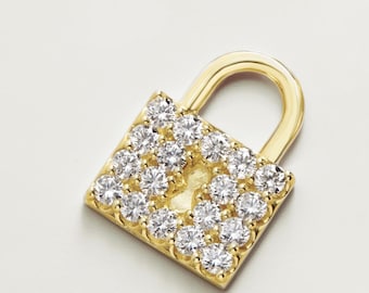 May include: A gold-colored padlock pendant encrusted with numerous clear, sparkling gemstones. The pendant has a square body and a curved handle, set against a white background. The gemstones are arranged to cover the front of the padlock.