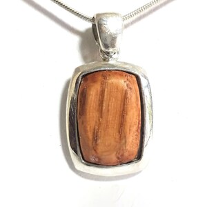 May include: A silver pendant necklace with a rectangular wooden inlay. The wood has a natural brown color and a striped pattern.