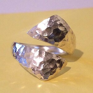 Puede incluir: Un anillo de metal martillado plateado con un diseño abierto único. El anillo está hecho de dos piezas que se envuelven alrededor del dedo.