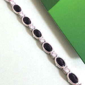 May include: A silver bracelet with black oval stones and clear round stones.