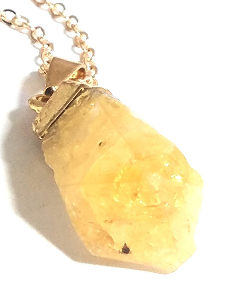 K&ouml;nnte beinhalten: Eine goldene Kettenkette mit einem gelben Kristallanh&auml;nger. Der Kristall ist facettiert und hat ein raues, nat&uuml;rliches Aussehen.