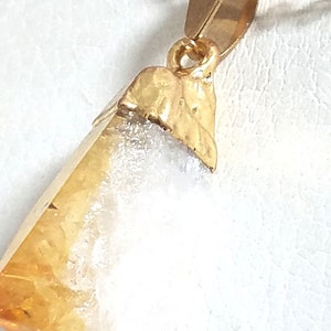 K&ouml;nnte beinhalten: Eine goldene Halskette mit einem Anh&auml;nger aus einem rohen, nat&uuml;rlichen Citrin-Kristall mit einem wei&szlig;en, wolkigen Inneren. Der Kristall ist in einer goldenen Fassung gefasst und h&auml;ngt an einer zarten goldenen Kette.