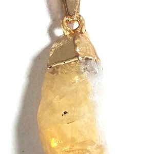 K&ouml;nnte beinhalten: Eine goldene Kettenkette mit einem rohen, gelben Citrin-Anh&auml;nger. Der Anh&auml;nger ist an einer goldenen &Ouml;se befestigt.
