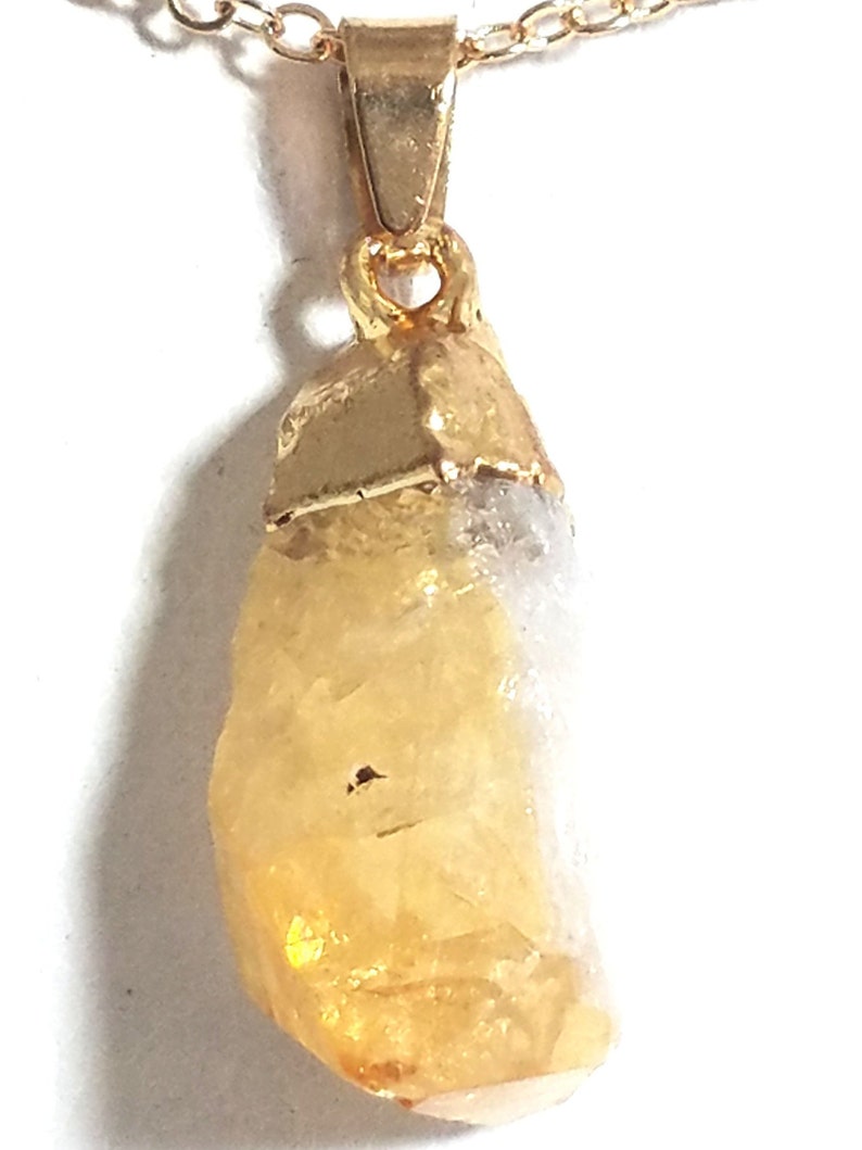 K&ouml;nnte beinhalten: Eine goldene Kettenkette mit einem rohen, gelben Citrin-Anh&auml;nger. Der Anh&auml;nger ist an einer goldenen &Ouml;se befestigt.