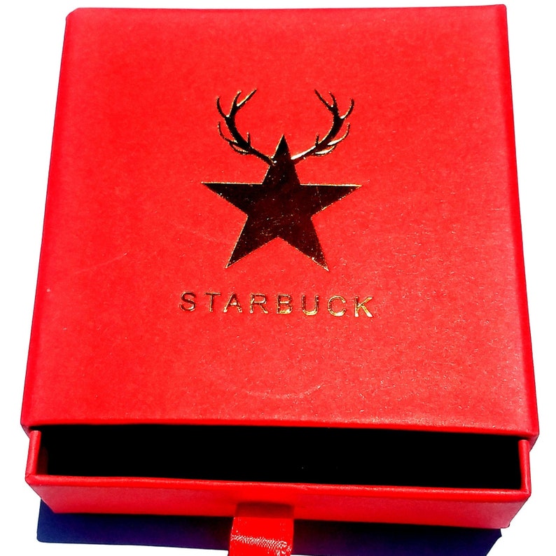 K&ouml;nnte beinhalten: Rote Box mit einem goldenen Stern und Geweih, und dem Wort "STARBUCK" auf der Vorderseite. Die Box hat eine Schublade, die ge&ouml;ffnet ist.