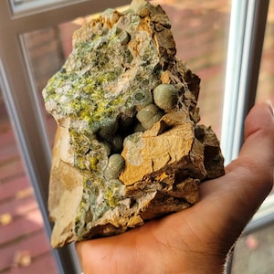 May include: A close-up of a rock formation with green and brown colors. The rock has a cluster of small, round, green stones embedded in it.
