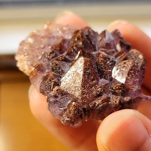 May include: A cluster of amethyst crystals with a deep purple hue and a metallic sheen. The crystals are arranged in a pointed formation, resembling a small mountain range.