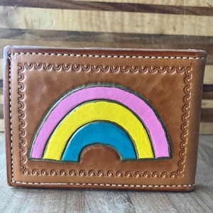 May include: A brown leather wallet with a rainbow design. The rainbow is made of pink, yellow, blue, and brown leather.