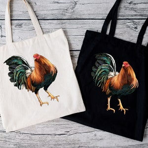 May include: Two tote bags, one cream and one black, each featuring a detailed illustration of a rooster. The rooster has brown, orange, green, and white feathers, a red comb, and yellow legs. The bags have long handles for carrying.