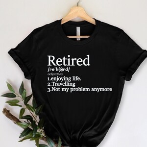 Pode incluir: Camiseta preta com a palavra "Aposentado" em branco, sua pronúncia e definição. A definição inclui "aproveitando a vida", "viajando" e "não é mais meu problema".