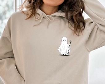 May include: Beige hoodie with a front pocket and drawstring. A black and white cartoon ghost holding a coffee cup is printed on the front. The ghost has a bored expression. The hoodie is made of a soft material.