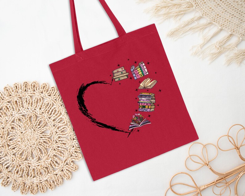 May include: A red tote bag featuring a black heart shape with a stack of books and open books with flowers. The books are in various colors and styles. The tote bag has two red handles.