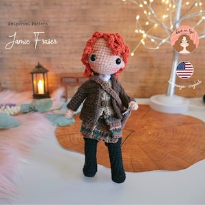 May include: Crocheted amigurumi doll with red hair, wearing a brown jacket, a plaid kilt, and black boots. The doll is standing on a wooden surface. The image includes the text "Jamie Fraser" and "Amigurumi Pattern".