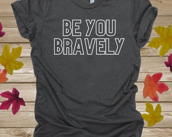 Op de afbeelding: Een donkergrijs T-shirt met de tekst "BE YOU BRAVELY" in wit.