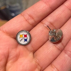 May include: A pair of silver earrings with a Steelers logo on one earring and a plain silver design on the other.