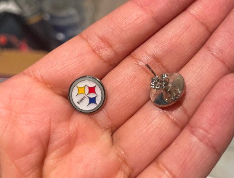 May include: A pair of silver earrings with a Steelers logo on one earring and a plain silver design on the other.