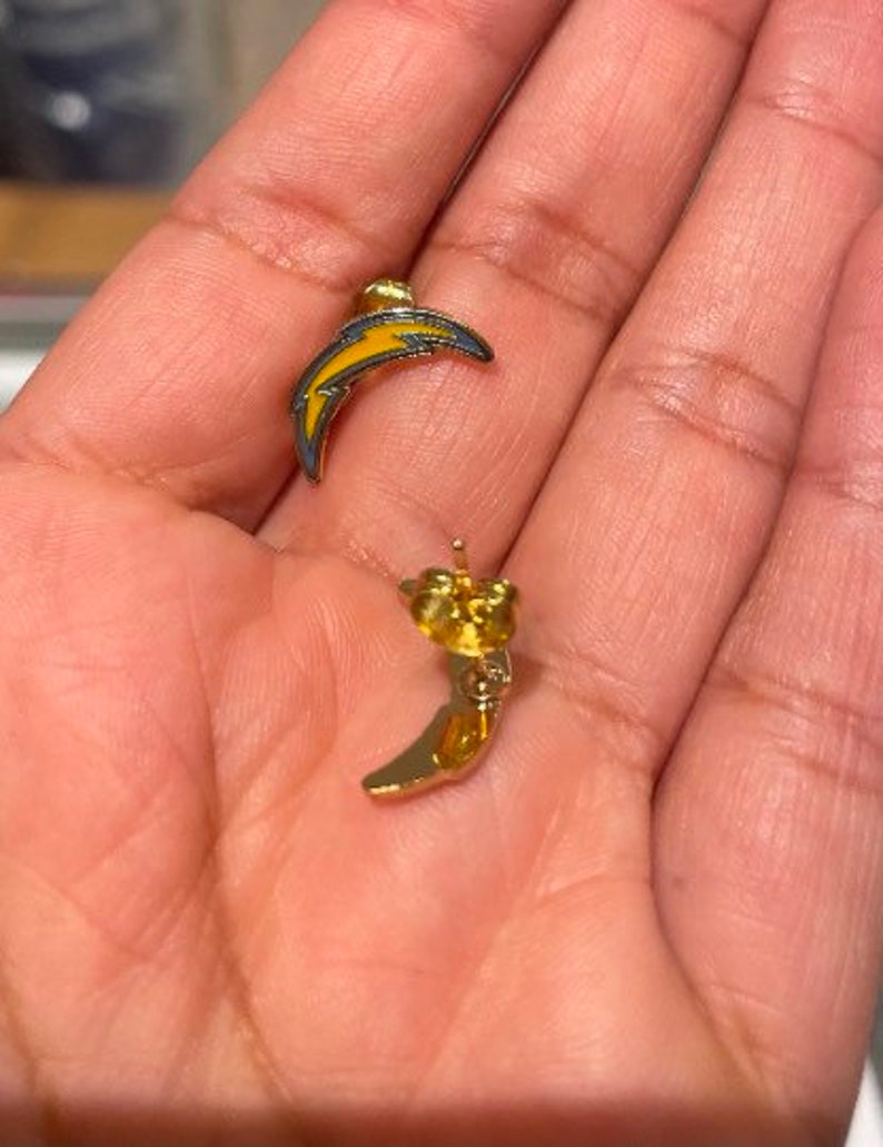 May include: A pair of gold earrings with a lightning bolt design. The earrings are yellow and blue.