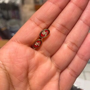 May include: A pair of gold cufflinks with red and white enamel. The cufflinks feature the letters "SF" in white on a red background.