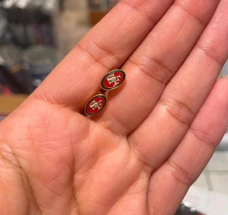 May include: A pair of gold cufflinks with red and white enamel. The cufflinks feature the letters "SF" in white on a red background.