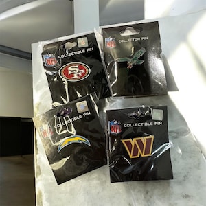 May include: Four NFL collectible pins on black cards. The pins feature the logos of the 49ers, Eagles, Chargers, and Commanders. Each pin is in a plastic sleeve and has a hang hole at the top.