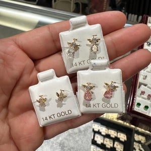 May include: Gold angel earrings with clear and pink gemstones, presented on white cards. Each card is labelled "14 KT GOLD". The earrings feature an angel design with wings and a halo.