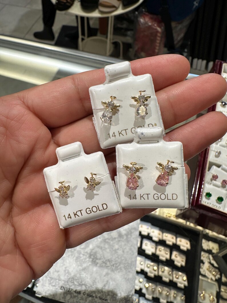 May include: Gold angel earrings with clear and pink gemstones, presented on white cards. Each card is labelled "14 KT GOLD". The earrings feature an angel design with wings and a halo.