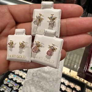 May include: Three pairs of 14 KT GOLD angel earrings. One pair features clear teardrop-shaped gems, another has pink pear-shaped gems, and the third has small clear gems. The earrings are displayed on white cards.