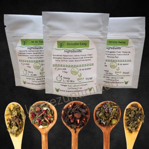 May include: Three small white pouches with green labels containing loose leaf tea blends. The labels have the names "Ni Ni Time", "Breathe Easy", and "Stress Away" with a list of ingredients and instructions for brewing. The pouches are sitting on a wooden surface with three wooden spoons filled with the tea blends.