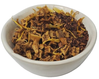 May include: A white bowl filled with a loose leaf tea blend. The tea blend contains dried apple pieces, dried flower petals, and brown tea leaves.