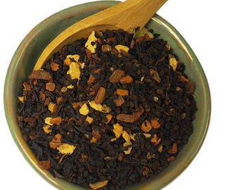 May include: A close-up of a green ceramic bowl filled with a blend of black tea, orange peel, cinnamon sticks, and other spices. The tea is ready to be brewed for a warm and flavorful beverage.