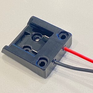 Peut inclure: Un support de batterie en plastique noir avec deux fils attach&eacute;s. Un fil est rouge et l'autre est noir.