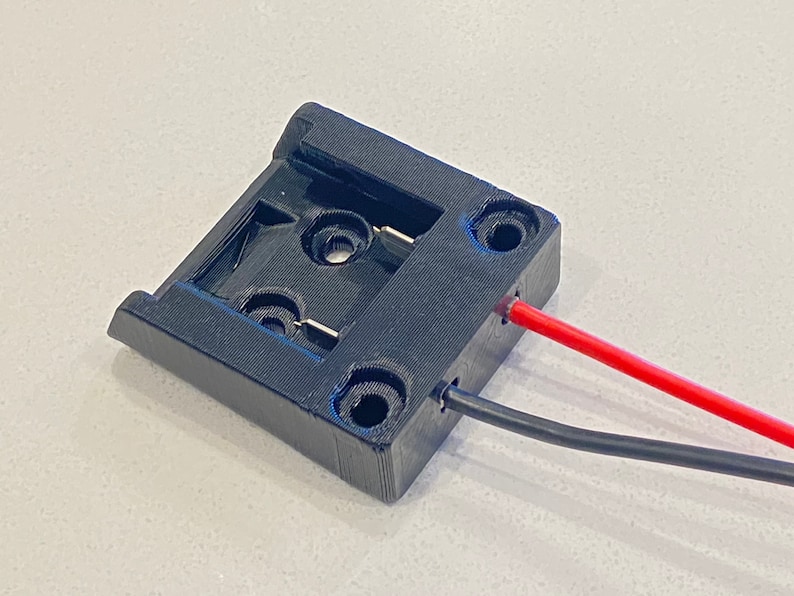 Peut inclure: Un support de batterie en plastique noir avec deux fils attach&eacute;s. Un fil est rouge et l'autre est noir.