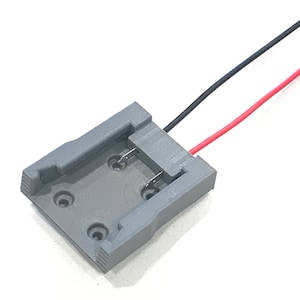 May include: A gray plastic battery holder with two wires attached. The wires are red and black. The holder has four holes for screws.