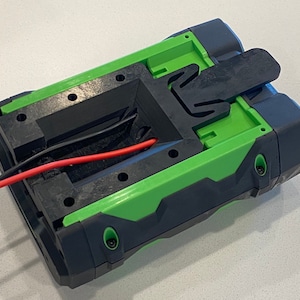 May include: A green and black battery pack with a black plastic latch. The battery pack has a red and black wire coming out of it.