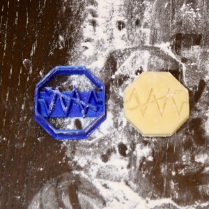 May include: A blue plastic cookie cutter shaped like a heart with a wavy line design. A cookie is shown next to the cutter, with the same design imprinted on it.