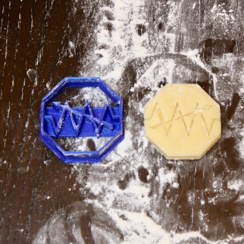 May include: A blue plastic cookie cutter shaped like a heart with a wavy line design. A cookie is shown next to the cutter, with the same design imprinted on it.