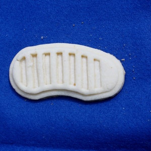 May include: A white cookie shaped like a footprint with a series of parallel lines embossed on the surface. The cookie is on a blue background.
