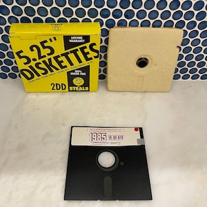 May include: A black 5.25 inch floppy disk labeled "Mastertronic 1985: The Day After Commodore 64 - Diskette". The disk is in a yellow box with the text "5.25" Diskette" and "2DD Steals".