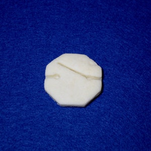 Può includere: Un oggetto ottagonale bianco sporco con un dettaglio di linea scolpita, su uno sfondo blu intenso. L'oggetto sembra essere fatto di un materiale naturale, forse pietra o osso.