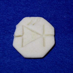 May include: A white, round, biscuit-like object with a triangular design embossed on the surface.