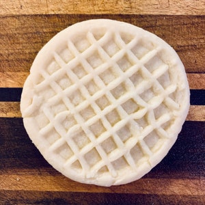 May include: A white waffle cookie with a grid pattern on top. The cookie is on a wooden surface.