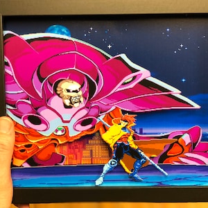 May include: A framed 3D pixel art print of a video game character, a red-clad superhero, fighting a giant, pink, mechanical monster. The background is a night sky with stars and a blue planet.