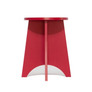 May include: A red, round-top stool with a triangular base. The stool has a simple, modern design.