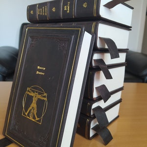 May include: A collection of hardcover books with dark brown covers and gold lettering. The titles include "The Walt Disney Prince" and "J.K. Rowling". Each book has a dark brown bookmark. The front book's cover features "Harry Potter" and a gold illustration.