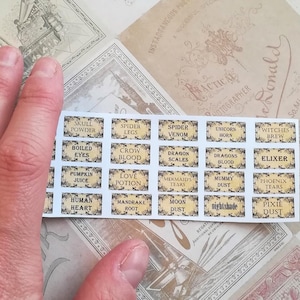 Puede incluir: Una hoja de pegatinas con varias etiquetas de pociones. Las etiquetas son amarillas con texto negro y tienen nombres como "Sangre de cuervo", "Escamas de dragón", "Lágrimas de sirena" y "Lágrimas de fénix".