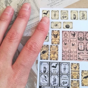 May include: A sheet of 16 black and white vintage-style labels with a Halloween theme. The labels feature images of bats, spiders, skulls, potions, and other spooky imagery. The labels are printed on white paper with a black border.