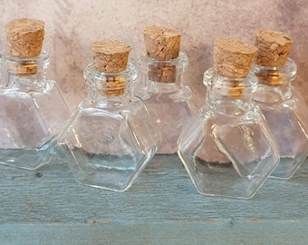 May include: Six small, clear glass bottles with cork stoppers. The bottles are hexagonal in shape and have a vintage look.