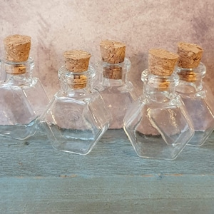 May include: Six small, clear glass bottles with cork stoppers. The bottles are hexagonal in shape and have a vintage look.