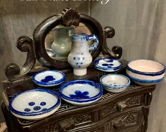 Puede incluir: Cerámica Vintage Bodo Hennig Salt Glaze. Juego de cerámica en miniatura con una jarra pequeña, cuencos y platos. La cerámica es blanca con detalles azules. El conjunto se exhibe en una cómoda de madera oscura con un espejo.