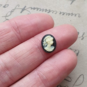 May include: A small oval cameo featuring a white profile of a woman with a black background.